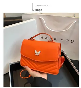 Close-up of orange crossbody bag featuring chevron stitching and a white butterfly clasp