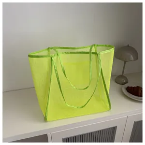 Detalle de un bolso tote grande de malla verde neón sobre una superficie blanca moderna