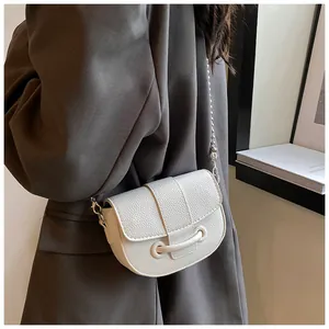 Gros plan d'un sac selle en cuir grainé blanc avec chaîne porté par un mannequin en costume