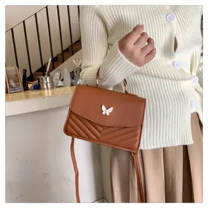 Brown quilted crossbody bag with butterfly buckle shown on a model in a cozy cafe setting