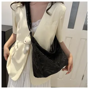 Detail of black pleated tote bag with a cute white plush bear pendant and wide shoulder strap
