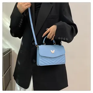 Detail of light blue crossbody bag with white butterfly buckle and V-shaped stitching