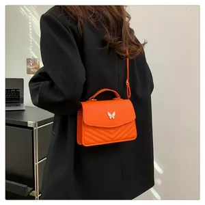 Detail of orange quilted crossbody bag with butterfly buckle on black suit model