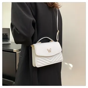 Close-up of a white quilted crossbody bag with metal butterfly buckle and model detail