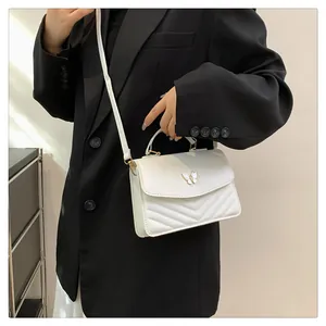 Chic white quilted crossbody bag with golden butterfly clasp shown on black blazer