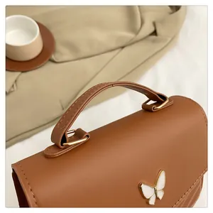Close-up of brown leather handbag featuring a white butterfly clasp and gold hardware