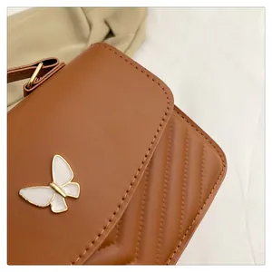 Detail of caramel PU leather bag with white enamel butterfly buckle and V-quilted stitching