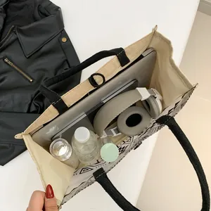 Large geometric tote bag in cream canvas with black straps holding a laptop and headphones