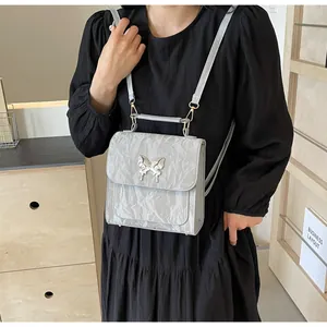 Detail of silver pleated texture handbag featuring a metallic butterfly emblem and handle