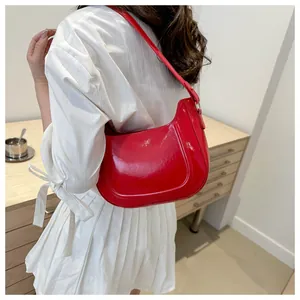 Red glossy patent leather hobo bag worn on shoulder by model with white skirt