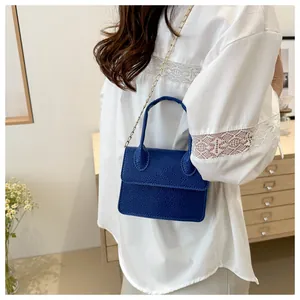 Détail du sac à main bleu foncé à texture litchi avec chaîne et haut en dentelle blanche