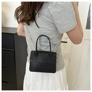 Détail d'un mini sac à main noir classique avec bandoulière dorée porté par un mannequin