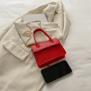 Mini sac à main rouge en cuir litchi avec chaîne dorée à côté d'un smartphone
