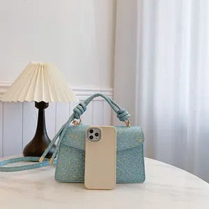 Glossy light blue sequin handbag with gold hardware and woven handle, shown with smartphone