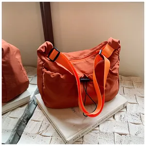 Detail of orange ruched nylon crossbody bag with adjustable strap and drawstring closure