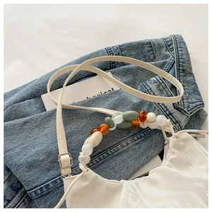 Detail of white pleated cloud bag featuring colorful bead handle and ripple texture