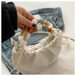 Detail of white pleated cloud bag featuring colorful chunky bead handle and leather strap