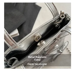 Detail of silver handbag featuring a magnetic snap closure and metallic chain strap