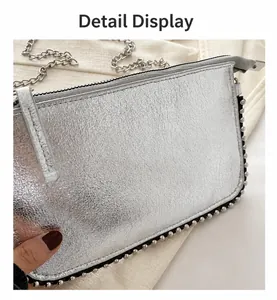Detalle de bolso plateado con cadena, textura metálica plisada y bordes con remaches