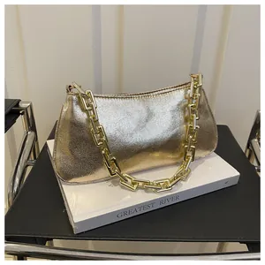 Detail of metallic gold shoulder bag with thick chain handle on a white book