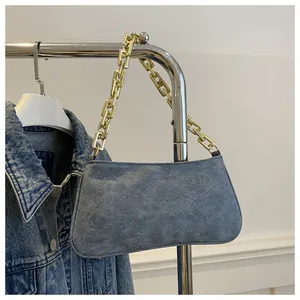 Detail of blue suede underarm bag with thick gold chain strap on a metal hanger