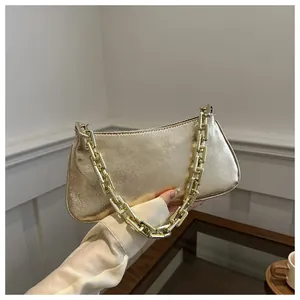 Detail shot of golden textured baguette bag with thick chain handle held by hand