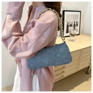 Detail of retro blue denim underarm bag featuring a bold chunky gold chain strap