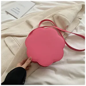 Détail d'un sac bandoulière en forme de fleur rose avec surpiqûres sur tissu blanc
