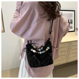 Detail of black pleated bucket bag with decorative colorful marble bead handle and drawstring