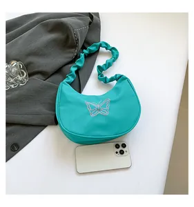 Detail of turquoise shoulder bag featuring pink embroidered butterfly and pleated strap