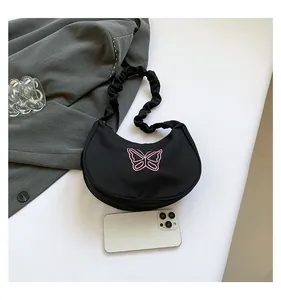 Detail of butterfly embroidery on black crescent bag with ruffled handle and smartphone for scale