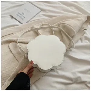 Vue rapprochée d'un sac à bandoulière en cuir blanc en forme de fleur sur un blazer beige