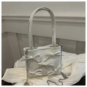 Detail of white handbag with 3D bows and silver bead chain on pleated fabric