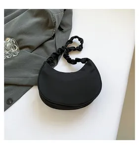 Detail of black crescent shoulder bag featuring a pleated strap and minimalist nylon design