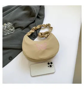 Close-up of beige half-moon bag featuring pink butterfly embroidery and ruched handle