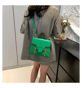 Detalle de bolso silla verde con estampado de cocodrilo, asa marrón y remaches