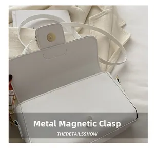 Detail view of the white crossbody bag featuring a golden magnetic hardware closure