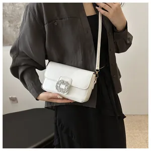 Close-up of white glossy crossbody bag featuring a sparkling crystal buckle on model