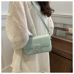 Detail of mint green small crossbody bag with rhinestone buckle worn by a model