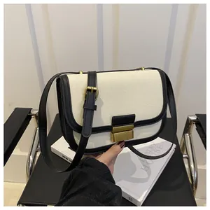 Detail of canvas shoulder bag featuring black leather trim and gold metal flip-lock