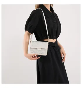 Dettaglio di una borsa a tracolla color crema con strass e sottile cinturino in pelle
