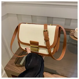 Detail of a retro cream canvas saddle bag with brown leather trim and golden metal clasp