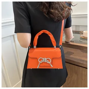 Nahaufnahme der leuchtend orangen Umhängetasche mit silberner Schleife und Rüschengriff