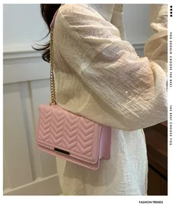 Detail of light pink quilted crossbody bag with gold chain strap on female model