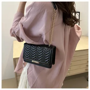 Detail of black chevron quilted crossbody bag with gold chain strap worn by a model
