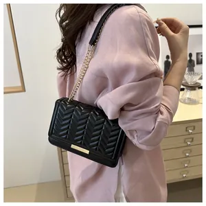 Minimalist black quilted crossbody bag with gold chain strap on model in indoor setting