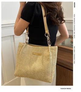 Detalle de bolso tote de paja dorada con correa de cadena metálica y logo de moda central