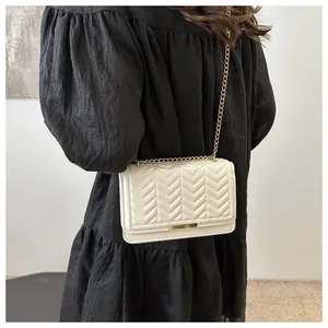 Detail showing white chevron quilted crossbody bag with gold chain strap on black dress