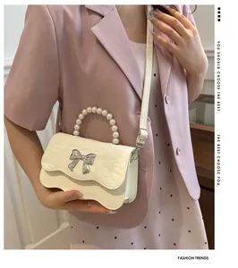 Detailed view of cream crossbody bag with pearl handle and silver metal butterfly bow