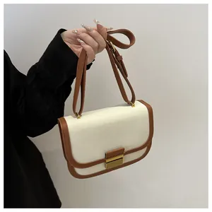 Detail of a color-block saddle bag with canvas body, leather trim, and golden lock